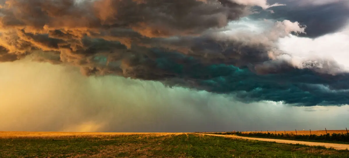 Dramatic storm clouds pass over a rural landscape as the sun sets on the horizon.