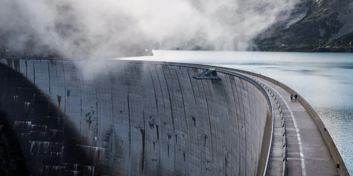 Massive dam wall in the middle of a mountain range, surrounded by clouds.
