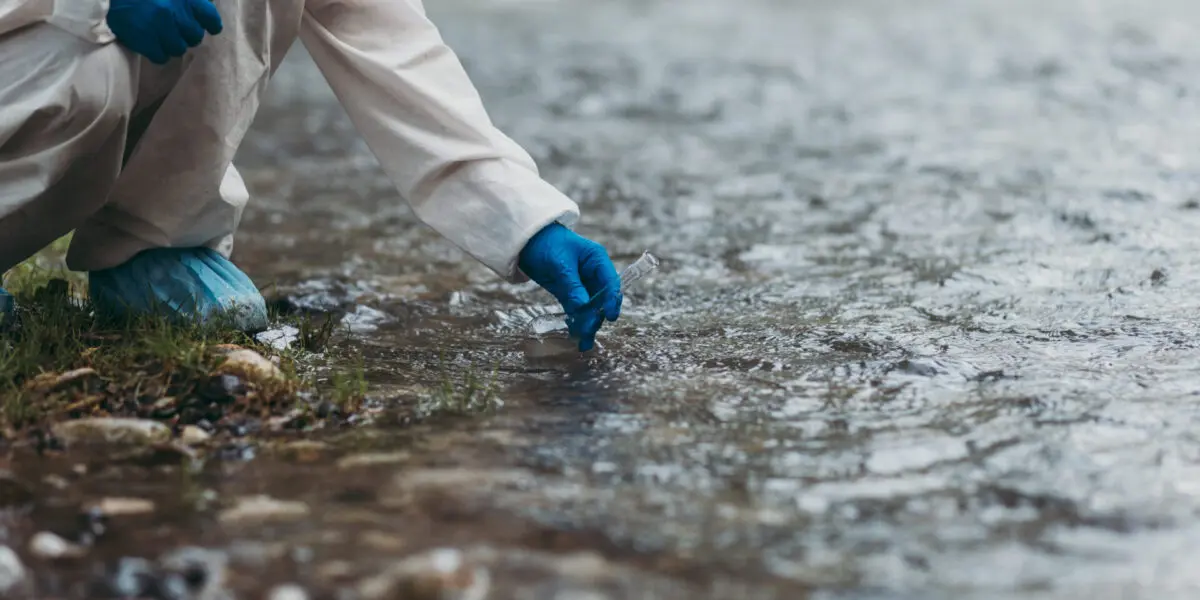 Scientist in a protective suit takes water samples from a river for ecological analysis.