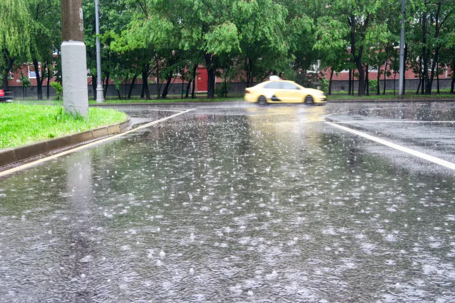 Heavy rain with hail in the city on a summer's day, large puddles on the wet carriageway.