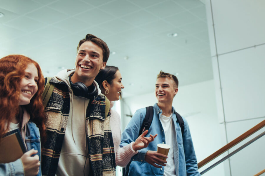 Eine Gruppe junger Menschen geht lachend und sich unterhaltend durch ein modernes, großes Gebäude.