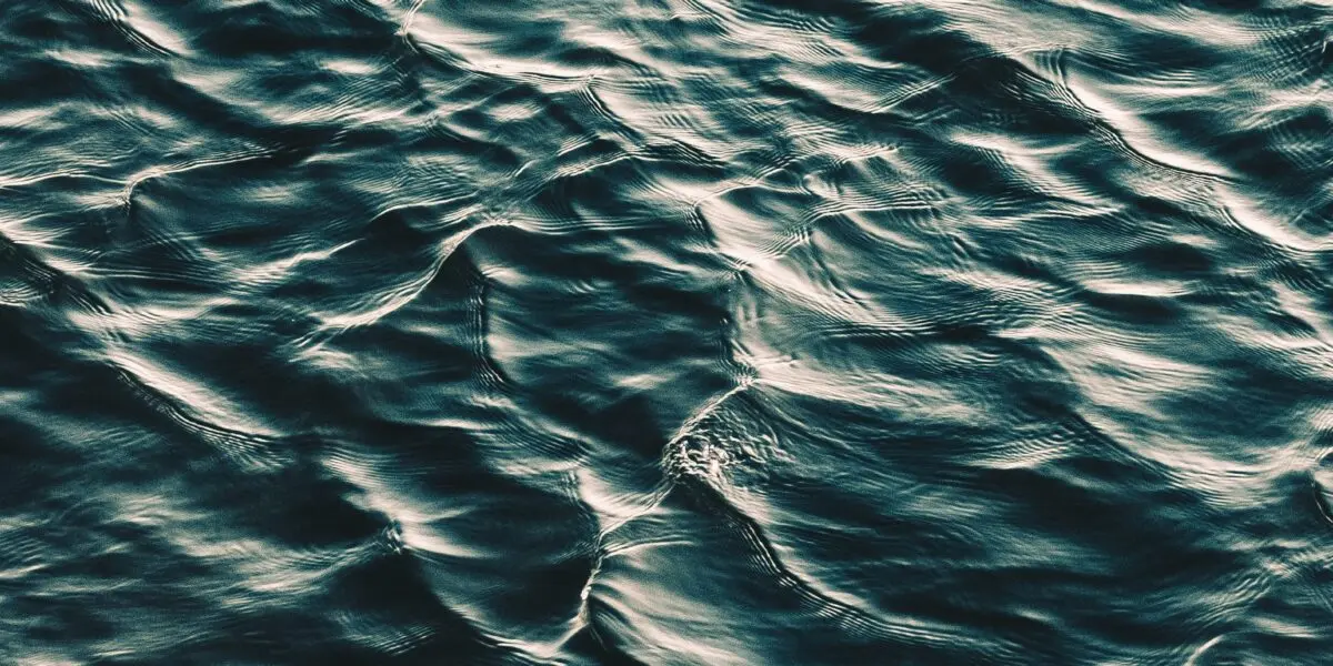 Sunlight reflects off gentle ripples on the surface of dark blue-green water, creating a textured pattern of light and shadow.