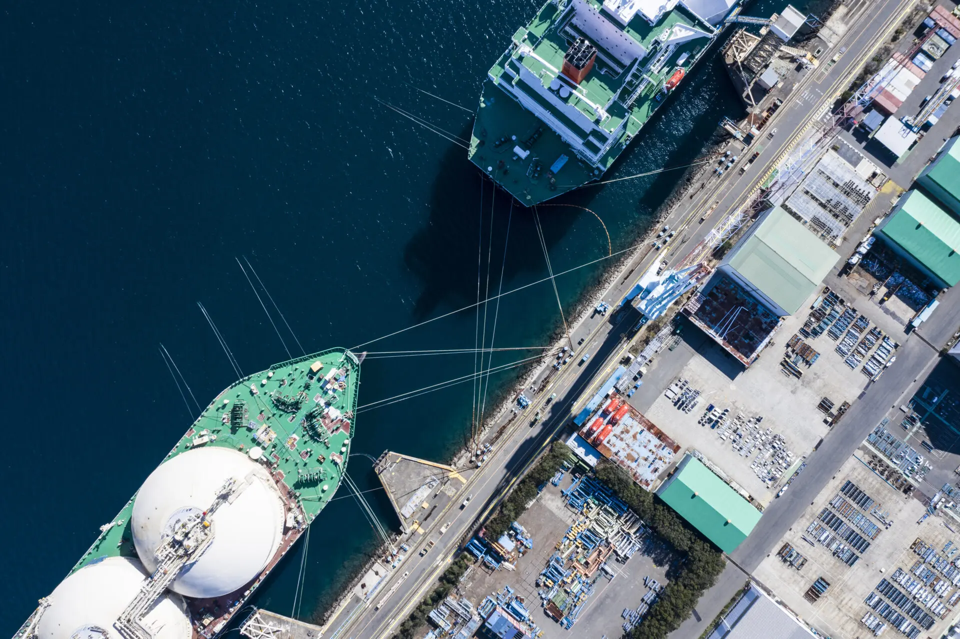Luftaufnahme eines großen Transportschiffs mit Treibstofftanks im Hafen, umgeben von einem weiteren Frachtschiff und einer Hafenanlage.