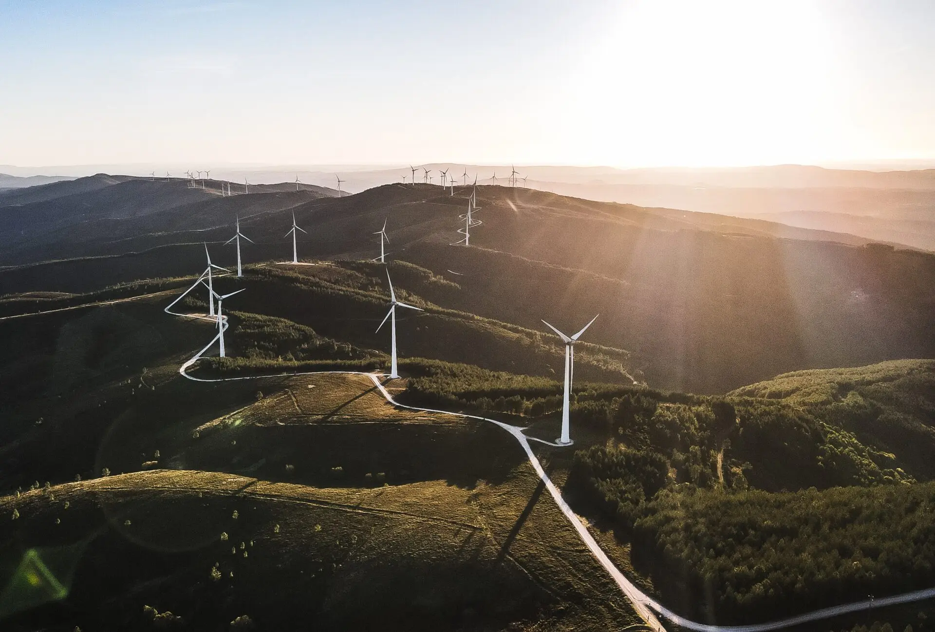 Windräder in einer hügeligen Berglandschaft unter strahlender Sonne – nachhaltige Energiegewinnung in der Natur.