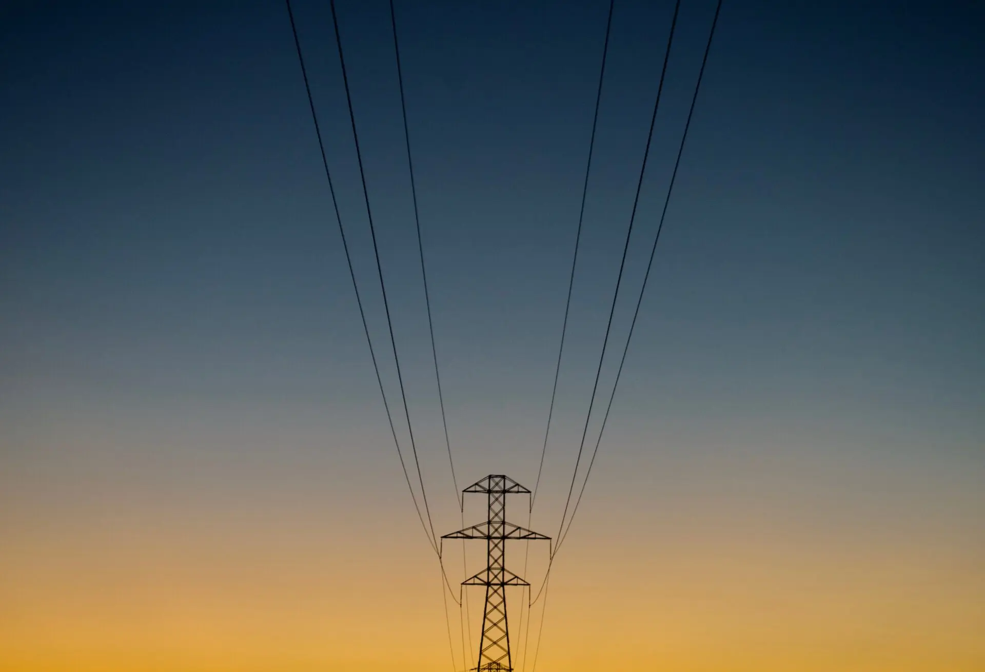 Ein Strommast mit Stromleitungen vor einem farbenfrohen Sonnenuntergang – Symbol für Energie und Infrastruktur.