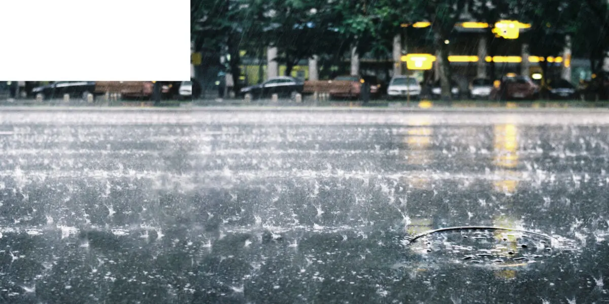 Heavy rain pours down on a street as water drains through a manhole cover.