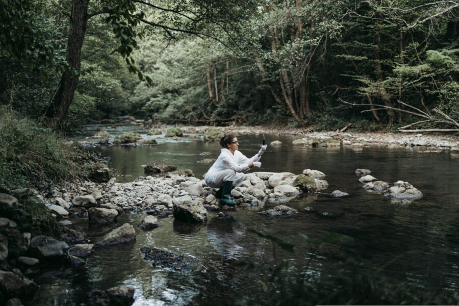 Scientist in protective clothing takes a water sample from a natural river to analyse the water quality.