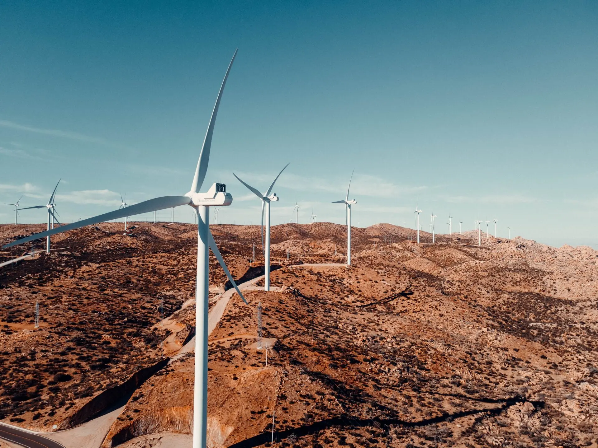 Windkraftanlagen auf einer hügeligen, trockenen Landschaft unter blauem Himmel – nachhaltige Energieerzeugung in der Natur.