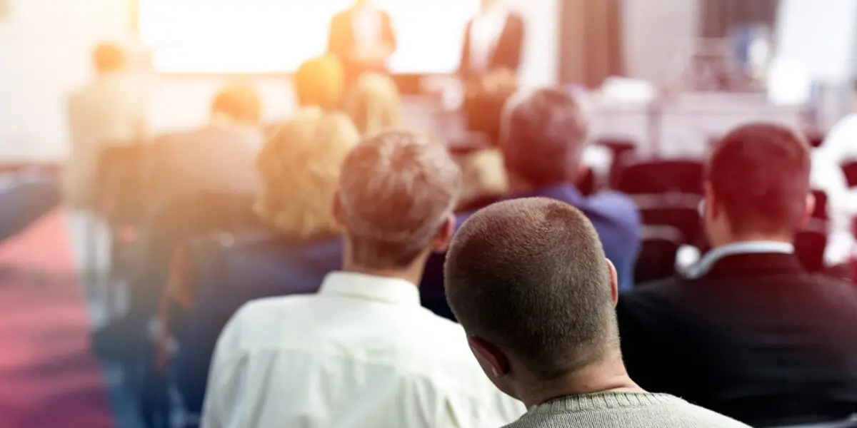 A presentation in a boardroom with a large audience during a conference.