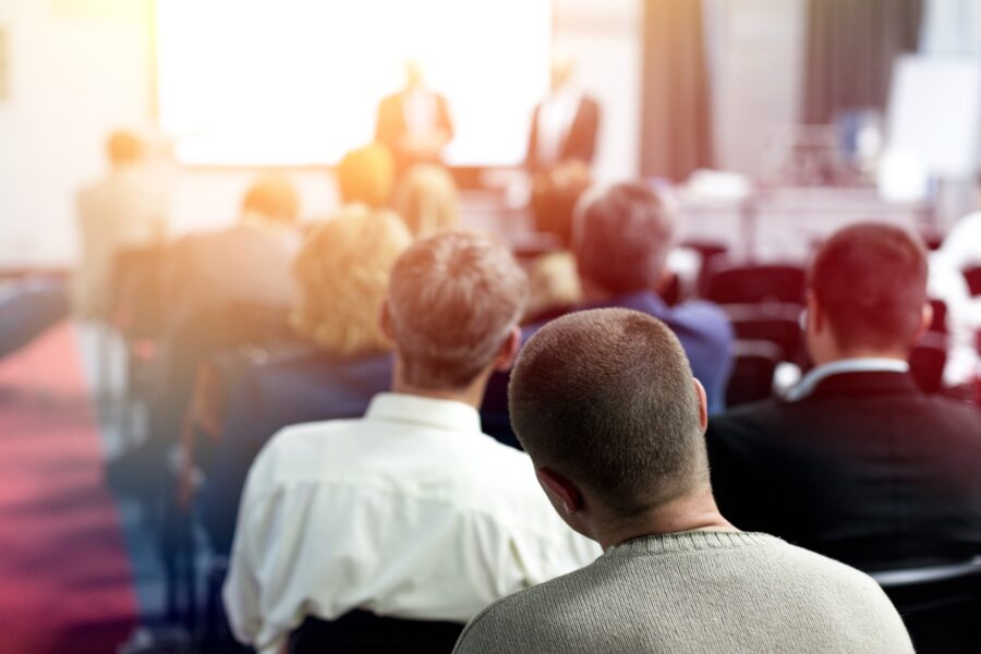 Ein Vortrag in einem Sitzungssaal mit vielen Zuhörern während einer Konferenz.