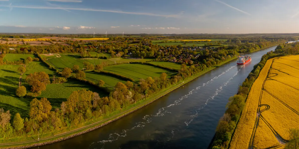 Cargo ship travelling on the Kiel Canal along blooming fields and green countryside.