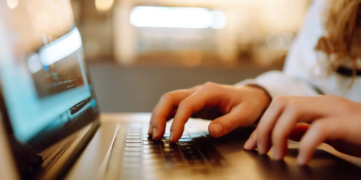 A female hand types on the keyboard of a laptop.