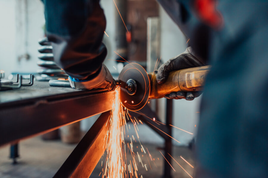Schlosser in Schutzkleidung und Schutzbrille bearbeitet Metall mit einem Winkelschleifer, während Funken sprühen.