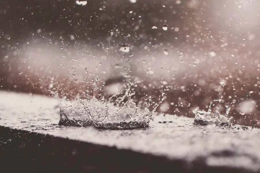 Nahaufnahme von Regentropfen, die auf eine Oberfläche spritzen und Wasserkronen und in der Luft verstreute Tropfen erzeugen, mit unscharfem Hintergrund und sanfter Beleuchtung.