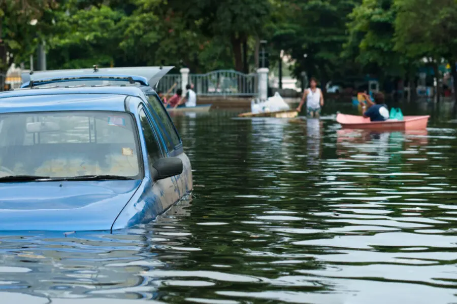 Ein Auto steht im Hochwasser, während Personen und Boote im Hintergrund zu sehen sind