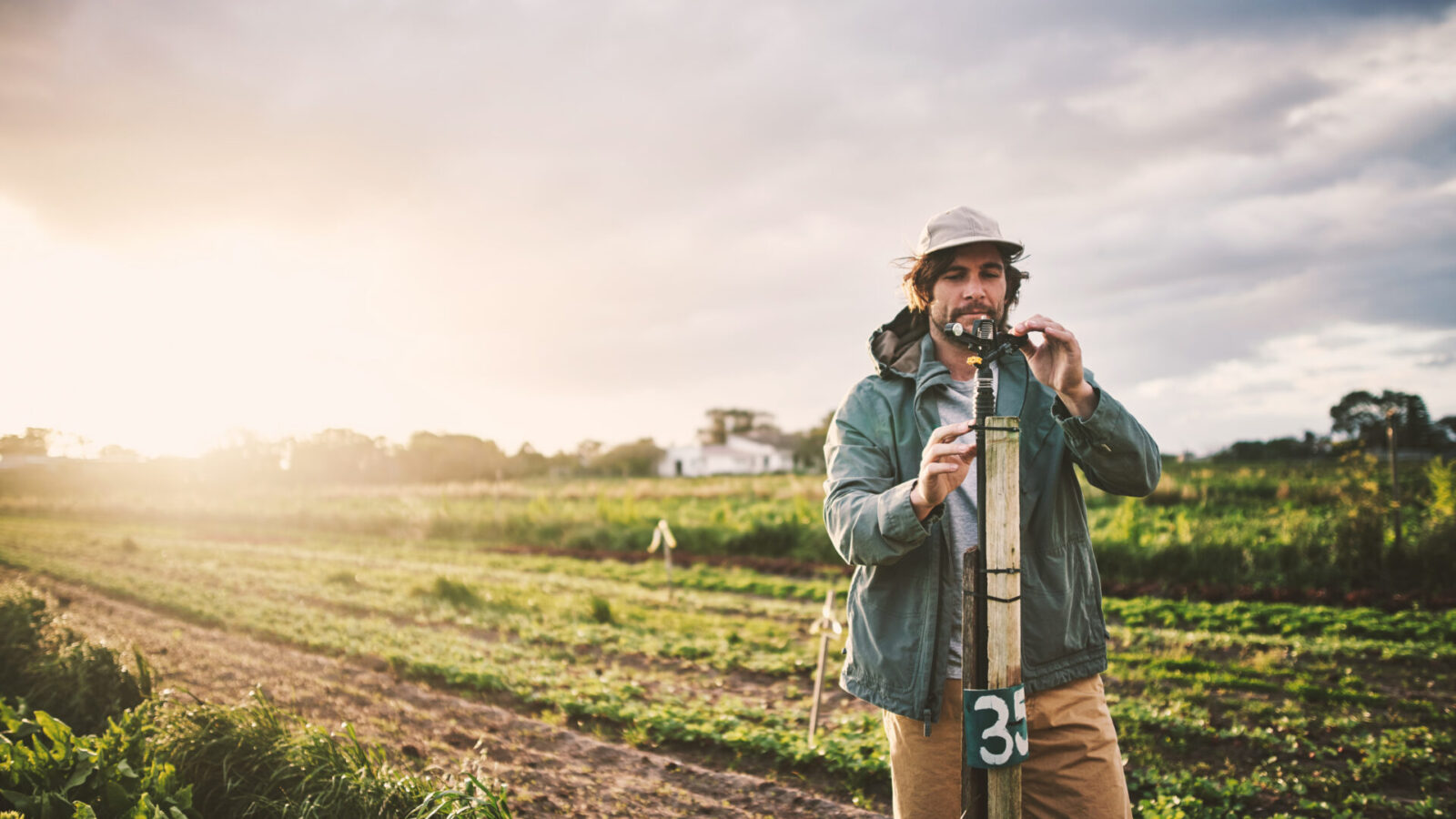 Junger Mann bedient eine Bewässerungsanlage auf einem Feld, um die Pflanzenbewässerung sicherzustellen.