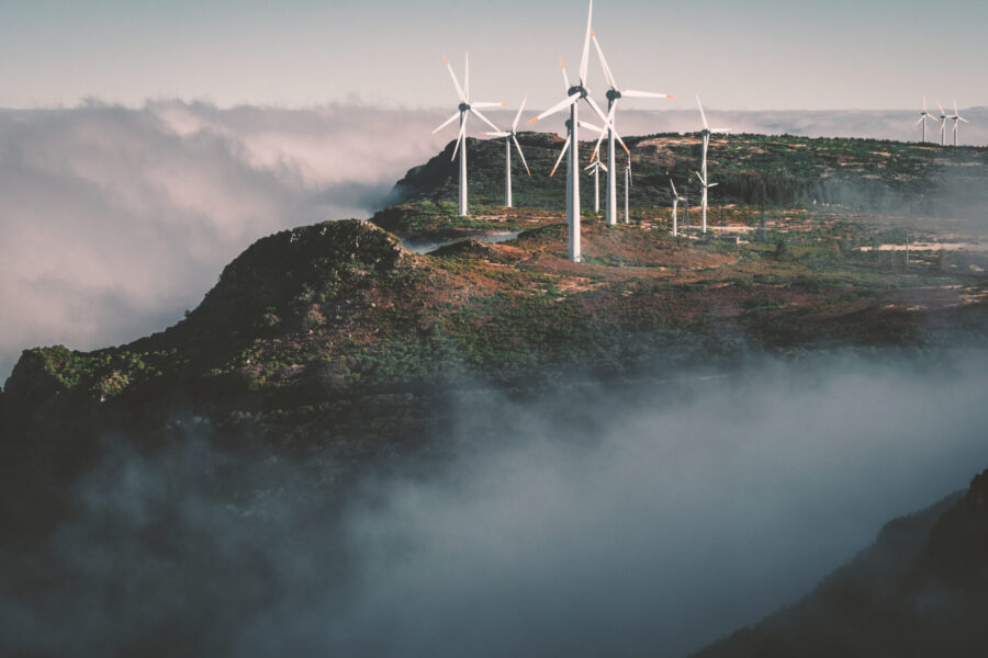 Eine Gruppe von Windrädern auf einem hohen Felsen, umgeben von Wolken.