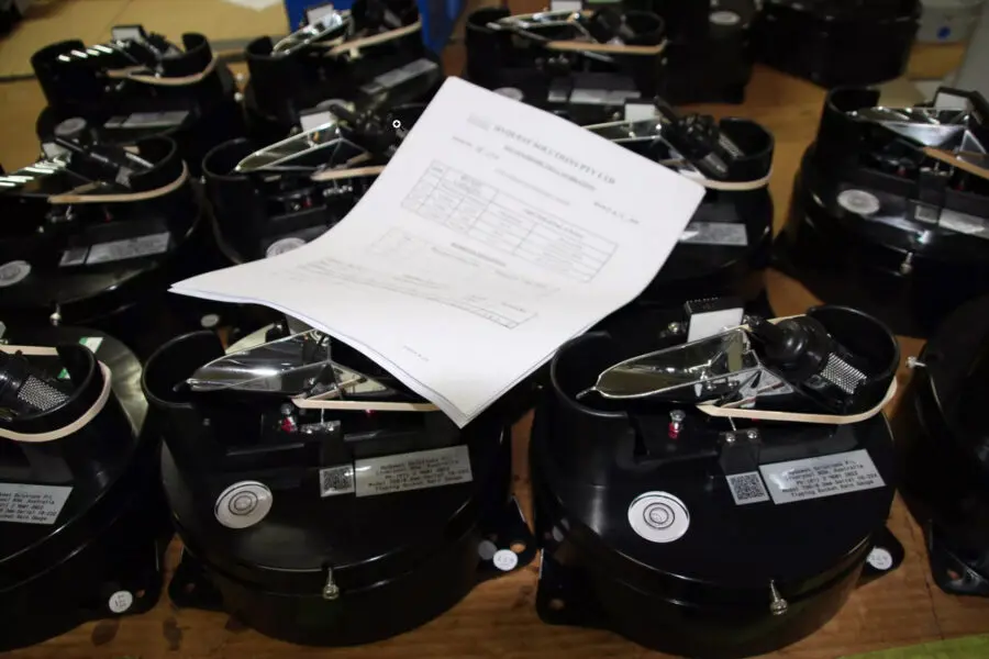 A stack of black mechanical devices with metallic components sits on a table, with a printed technical document or test sheet placed on top of one device in the foreground.