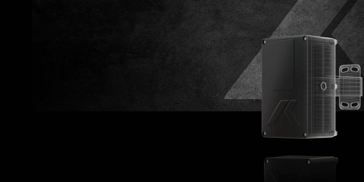 Ein schwarzes, rechteckiges elektronisches Gerät mit sichtbaren Schrauben an den Ecken wird vor einem dunklen, strukturierten Hintergrund mit geometrischen Mustern und Reflexionen gezeigt.