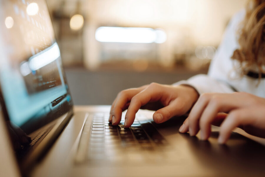 Nahaufnahme einer Person, die mit den Händen auf einer Laptop-Tastatur tippt, mit unscharfem Hintergrund.