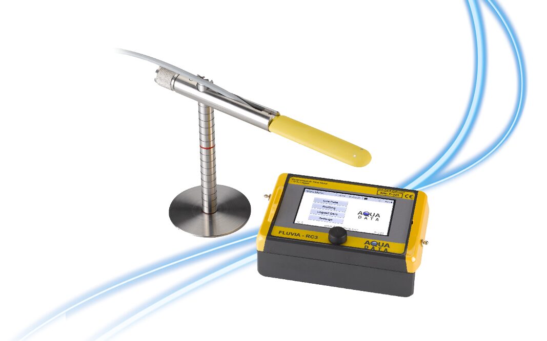 Eine Sonde mit gelbem Griff ist auf einem Metallständer neben einem kleinen, rechteckigen elektronischen Gerät mit einem Bildschirm mit der Aufschrift AQUA DATA FLUVIA-RCB angebracht. Im Hintergrund sind blaue gebogene Linien zu sehen.